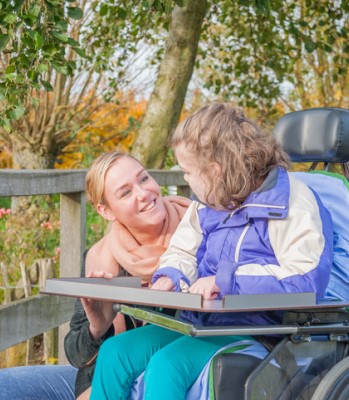 A young woman talks to a girl in an electric wheelchair in a park.